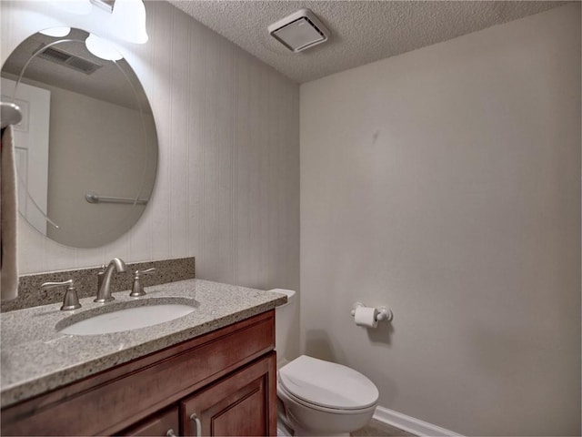 half bathroom featuring visible vents, a textured ceiling, vanity, and toilet