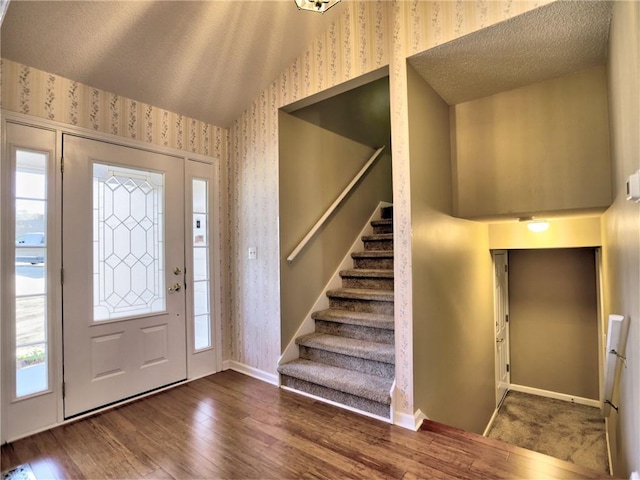 foyer featuring baseboards, wallpapered walls, lofted ceiling, and wood finished floors