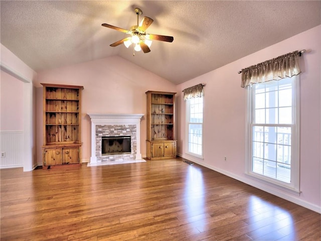 unfurnished living room with a stone fireplace, plenty of natural light, lofted ceiling, and wood finished floors