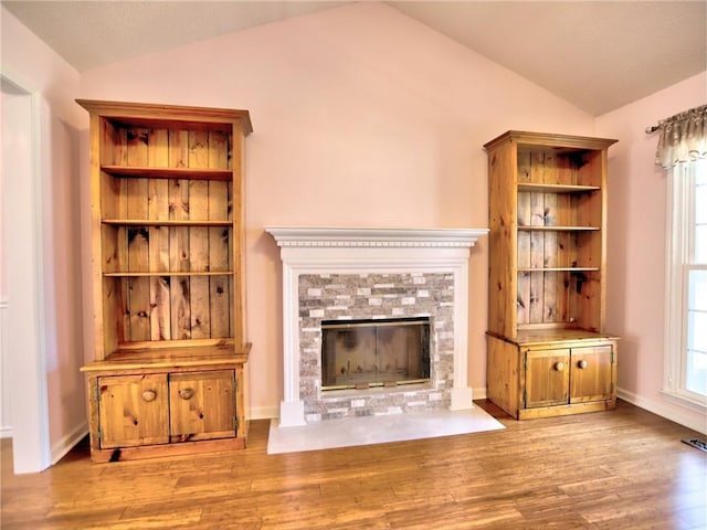 unfurnished living room featuring baseboards, a fireplace with flush hearth, wood finished floors, and vaulted ceiling