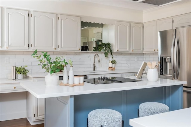 kitchen featuring light countertops, a kitchen bar, white cabinetry, stainless steel refrigerator with ice dispenser, and a sink