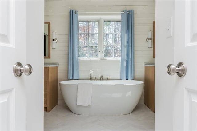 full bath featuring a soaking tub, tile walls, and vanity