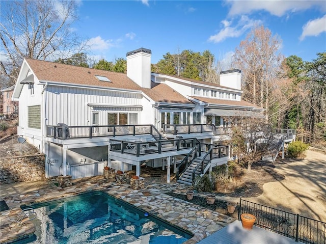 back of property with a deck, a patio, stairs, a fenced in pool, and a chimney