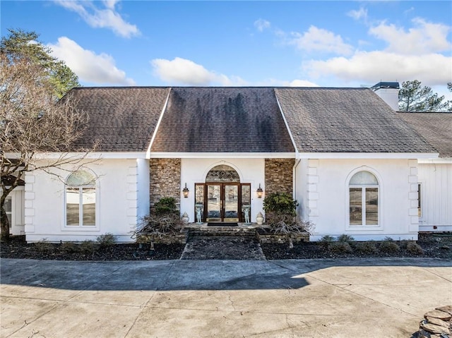 view of front of home featuring stone siding, a chimney, stucco siding, and french doors