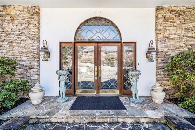 doorway to property with stone siding, french doors, and stucco siding