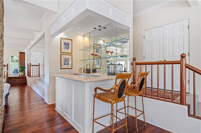 bar with dark wood finished floors, ornamental molding, beamed ceiling, stairs, and indoor wet bar