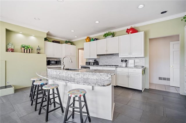 kitchen with a kitchen island with sink, a sink, visible vents, a kitchen breakfast bar, and white cabinets