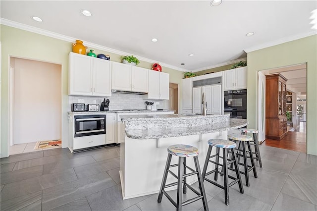 kitchen with dobule oven black, white cabinets, decorative backsplash, stainless steel microwave, and under cabinet range hood