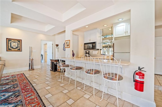 kitchen featuring black microwave, a raised ceiling, a kitchen bar, and freestanding refrigerator