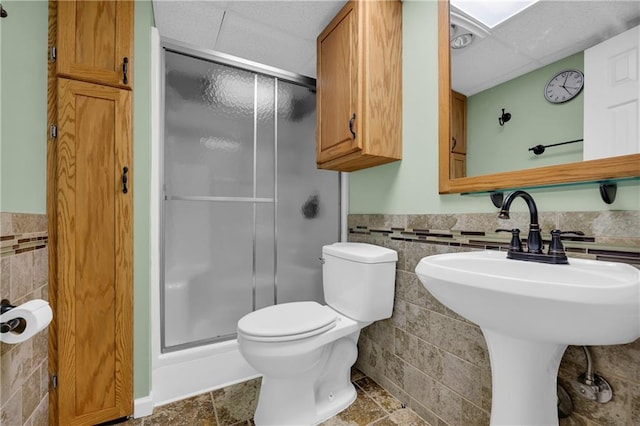 bathroom featuring tile walls, sink, toilet, and a shower with door