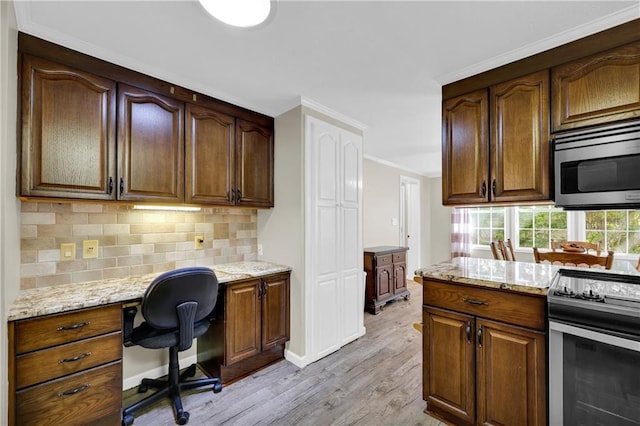 kitchen featuring stainless steel appliances, light hardwood / wood-style floors, built in desk, light stone counters, and ornamental molding