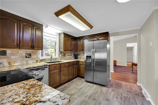 kitchen featuring tasteful backsplash, stainless steel appliances, light stone countertops, sink, and light hardwood / wood-style flooring