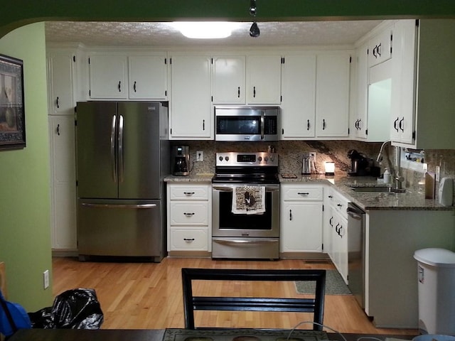 kitchen with light wood finished floors, a sink, stainless steel appliances, dark stone countertops, and backsplash