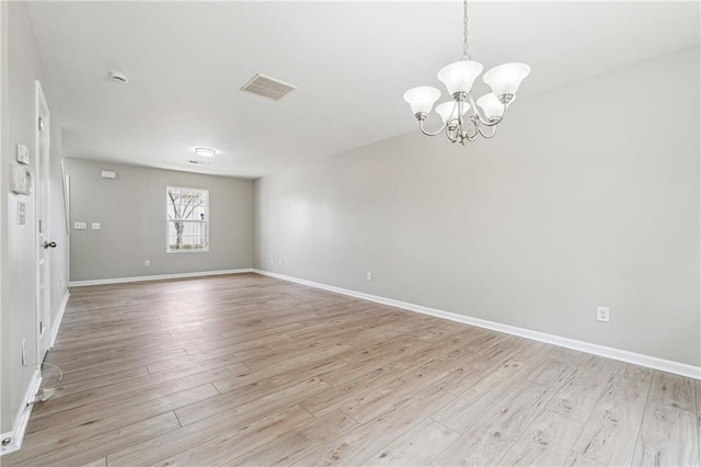 empty room featuring light wood-type flooring, an inviting chandelier, baseboards, and visible vents