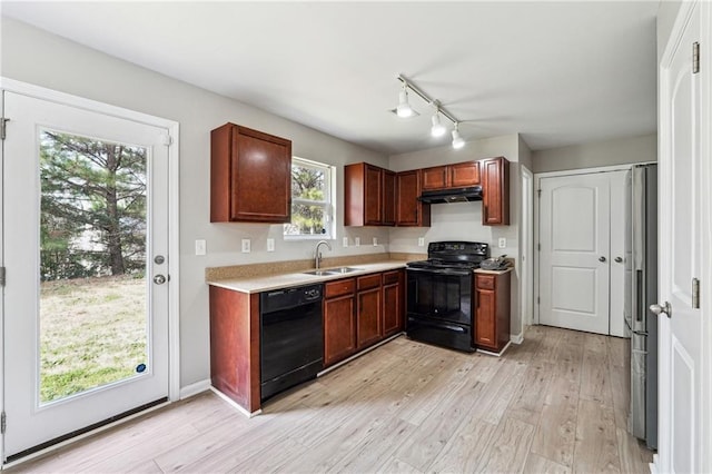 kitchen featuring light wood-style floors, under cabinet range hood, light countertops, black appliances, and a sink