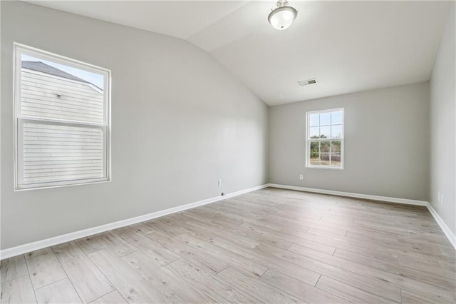 spare room featuring light wood-style floors, visible vents, vaulted ceiling, and baseboards