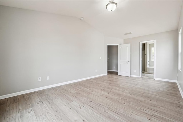 empty room featuring lofted ceiling, light wood-style flooring, visible vents, and baseboards