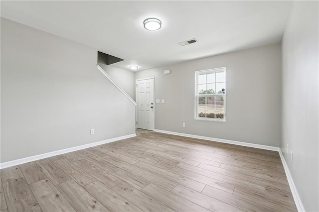 spare room with light wood-type flooring, visible vents, and baseboards