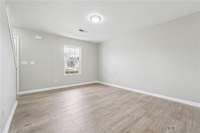 spare room with light wood-type flooring, visible vents, and baseboards