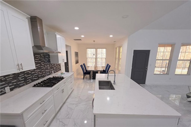 kitchen featuring a center island with sink, sink, wall chimney range hood, and gas cooktop