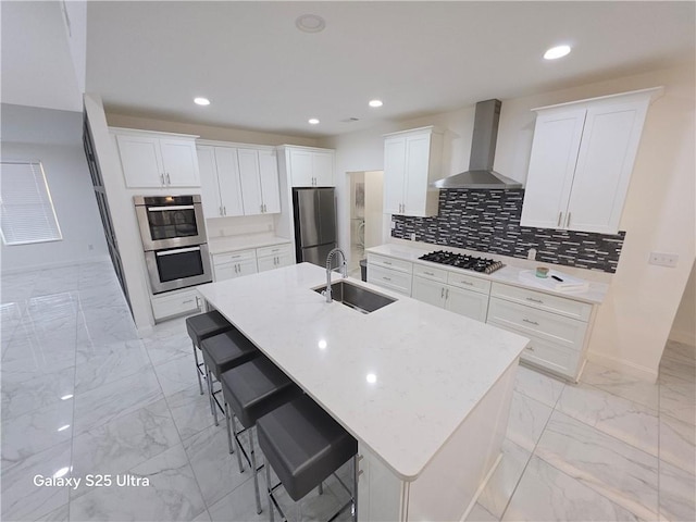 kitchen featuring appliances with stainless steel finishes, an island with sink, sink, a kitchen bar, and wall chimney range hood