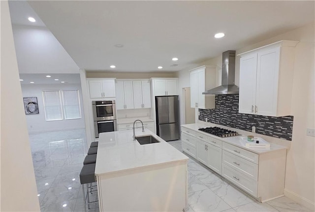 kitchen featuring sink, wall chimney range hood, an island with sink, stainless steel appliances, and white cabinets