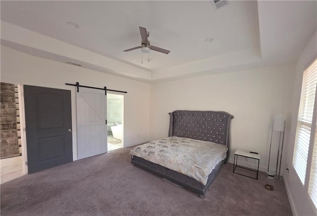 bedroom with ensuite bathroom, carpet floors, ceiling fan, a tray ceiling, and a barn door