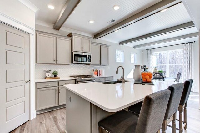 kitchen featuring beamed ceiling, a breakfast bar, gray cabinets, and appliances with stainless steel finishes