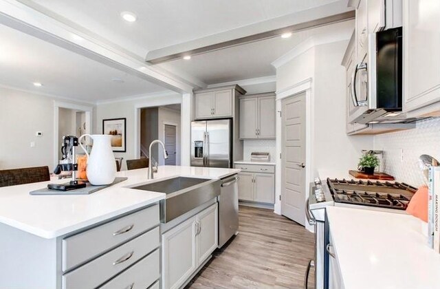 kitchen with sink, stainless steel appliances, decorative backsplash, a center island with sink, and light wood-type flooring