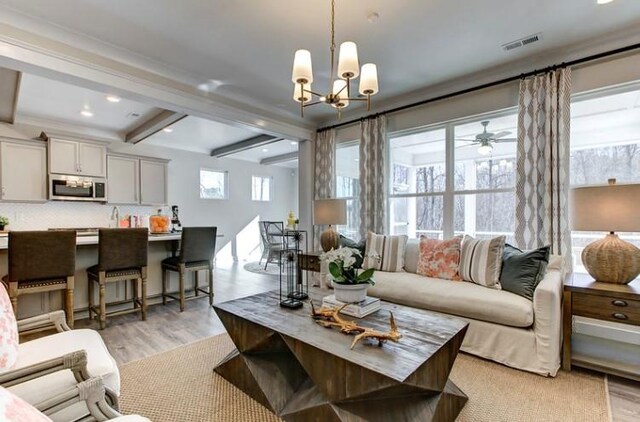 living room featuring beam ceiling, light hardwood / wood-style flooring, ceiling fan with notable chandelier, and ornamental molding