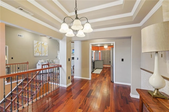 hall with a chandelier, dark wood-style flooring, visible vents, an upstairs landing, and a raised ceiling