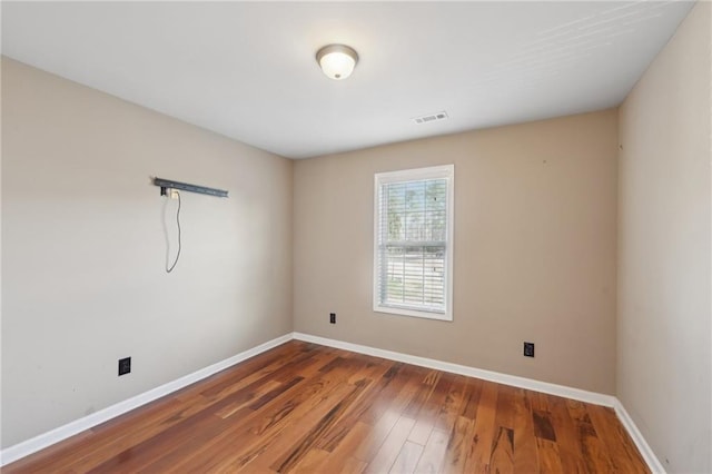 spare room with dark wood-style flooring, visible vents, and baseboards