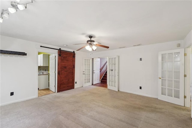 interior space with french doors, stairway, a barn door, a ceiling fan, and light carpet