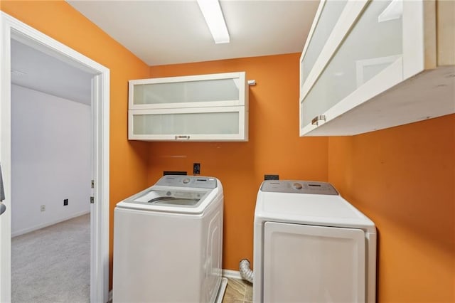 washroom with cabinet space, baseboards, separate washer and dryer, and light colored carpet