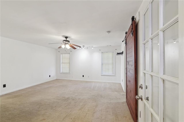 empty room featuring light colored carpet, ceiling fan, baseboards, and a barn door