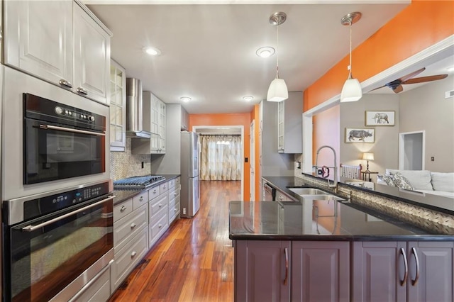 kitchen featuring a sink, white cabinets, wall chimney range hood, dark countertops, and glass insert cabinets