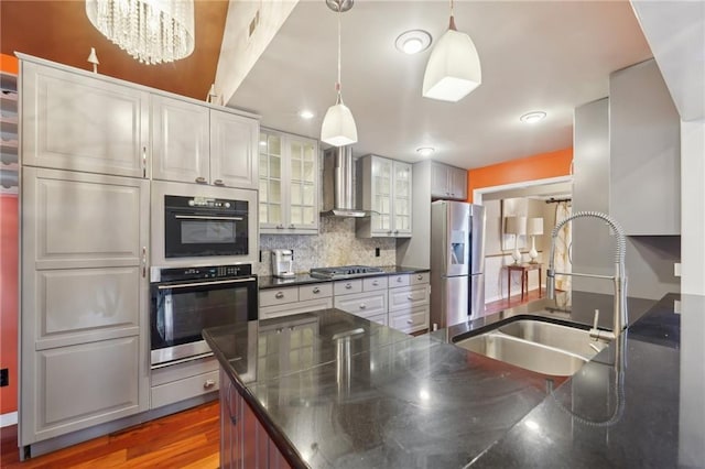 kitchen featuring glass insert cabinets, appliances with stainless steel finishes, hanging light fixtures, wall chimney range hood, and a sink