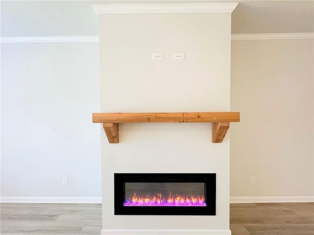 room details featuring a glass covered fireplace, crown molding, wood finished floors, and baseboards