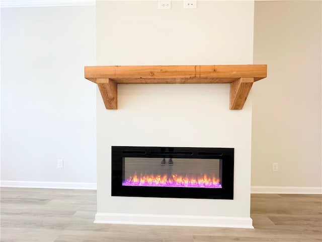 room details featuring a glass covered fireplace, baseboards, and wood finished floors