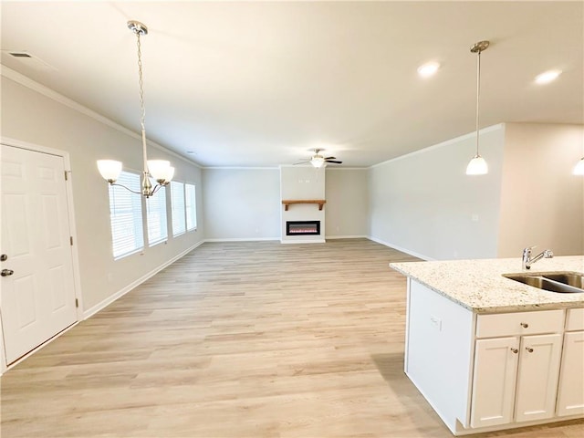 kitchen with a warm lit fireplace, a sink, light wood-style floors, crown molding, and ceiling fan with notable chandelier