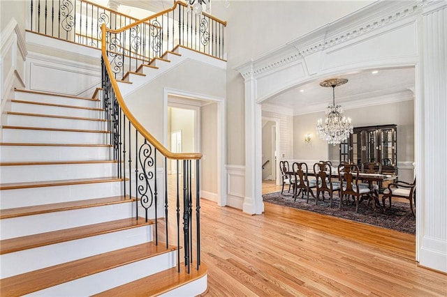 stairs with an inviting chandelier, crown molding, and wood-type flooring