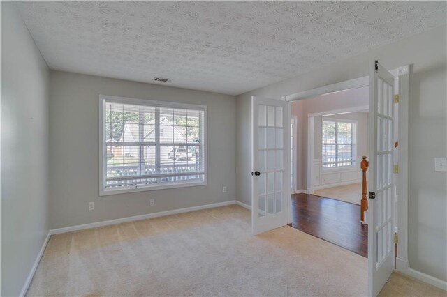 carpeted spare room with a textured ceiling and french doors