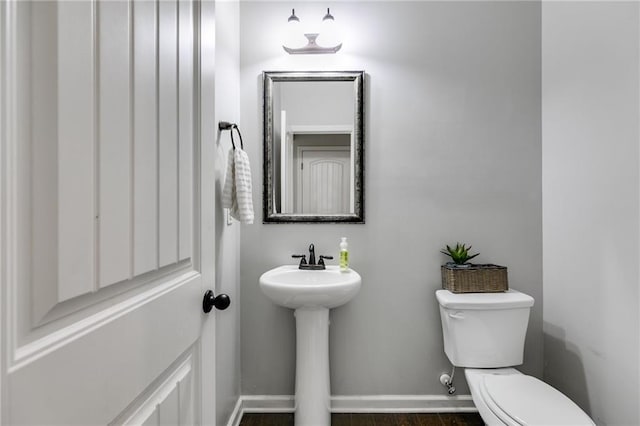 bathroom with toilet, baseboards, a sink, and wood finished floors