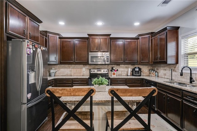 kitchen featuring appliances with stainless steel finishes, a sink, ornamental molding, dark brown cabinets, and light stone counters