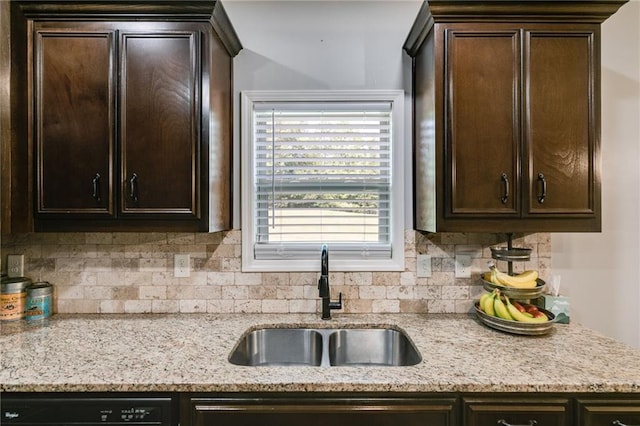 kitchen with a sink, dark brown cabinetry, decorative backsplash, and light stone countertops