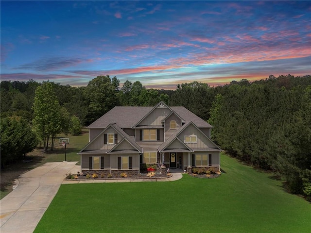 craftsman-style house featuring driveway, covered porch, a front yard, and stone siding
