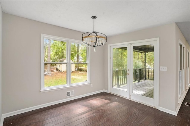 unfurnished dining area featuring visible vents, a healthy amount of sunlight, baseboards, a chandelier, and dark wood finished floors