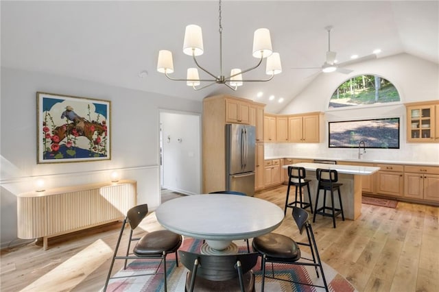 dining room featuring vaulted ceiling, ceiling fan with notable chandelier, light wood-type flooring, radiator, and sink