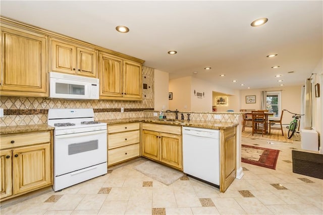 kitchen featuring a peninsula, white appliances, tasteful backsplash, and a sink