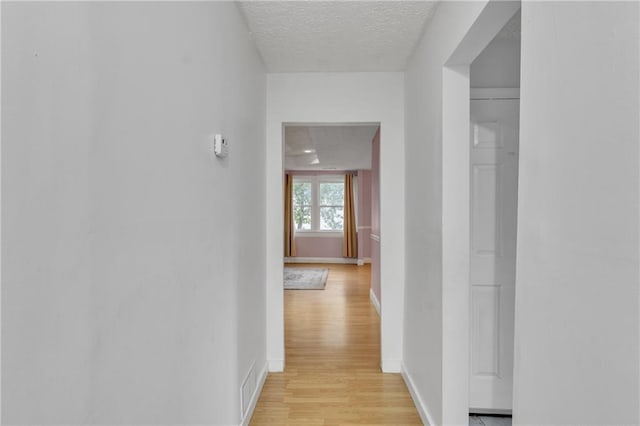 hall with a textured ceiling, visible vents, light wood-style flooring, and baseboards